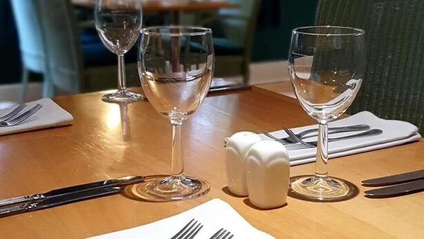 A dining table set with wine glasses, cutlery, and salt and pepper shakers, with chairs and a view of the city through large windows. - The Walnut Tree Hotel (Bridgwater)