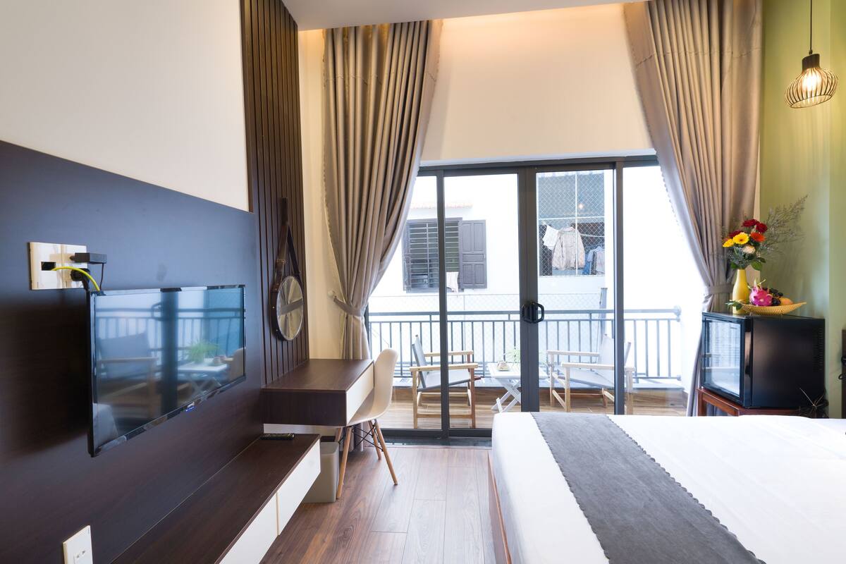 Ein Hotelzimmer mit Bett, Schreibtisch, Fernseher und einem Balkon mit Blick, sowie Vorhängen.