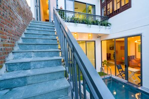 A staircase leading to a balcony with a pool, a brick wall, and a modern interior with a sofa and a table. - Le Printemps D' An Bang (Da Nang)