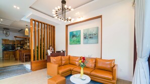 A modern living room with a sectional sofa, a round coffee table, and a decorative vase. - Le Printemps D' An Bang (Da Nang)