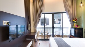 A hotel room with a bed, a desk, a TV, and a balcony with a view of the outside. - Le Printemps D' An Bang (Da Nang)