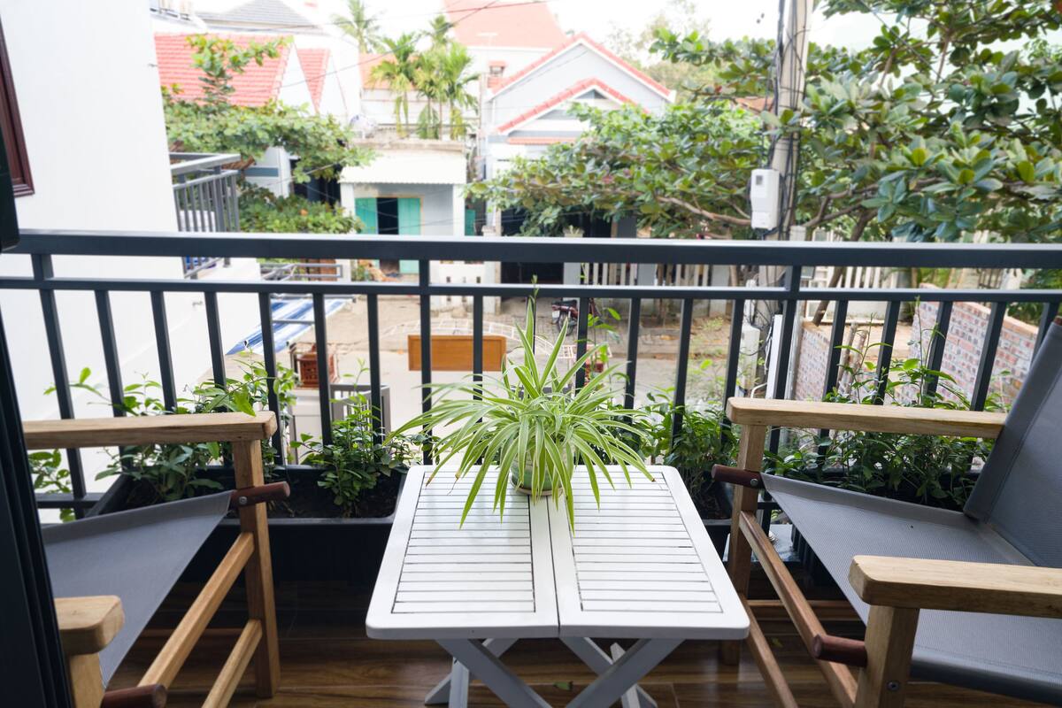 Ein Balkon mit Holztisch und zwei Stühlen, umgeben von Topfpflanzen.