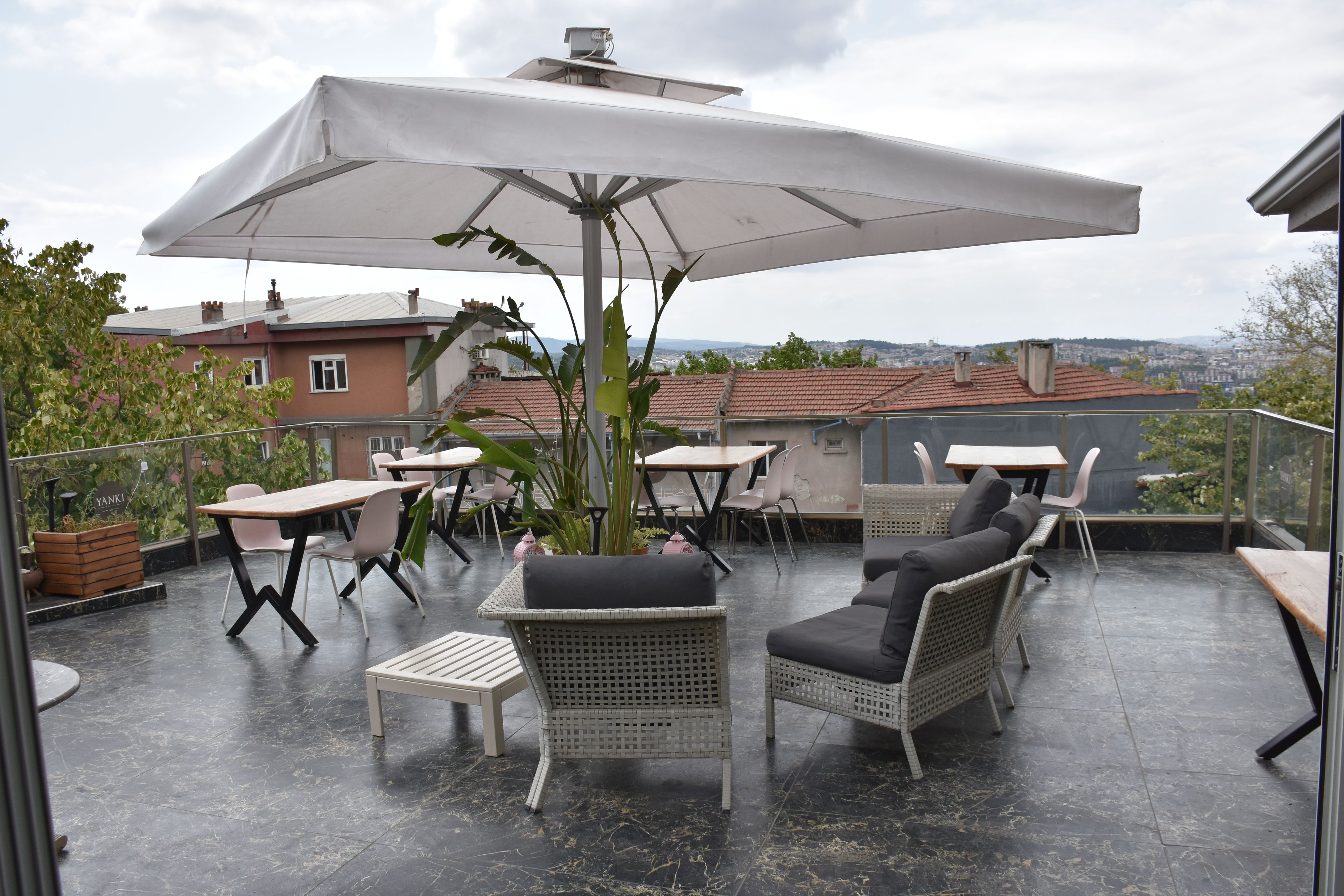 An outdoor patio with tables and chairs, a large umbrella, and a view of the cityscape.