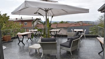 An outdoor patio with tables and chairs, a large umbrella, and a view of the cityscape.