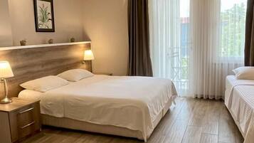 Habitación de hotel con una cama grande, mesitas de noche con lámparas, una silla roja y vistas al exterior a través de la ventana.