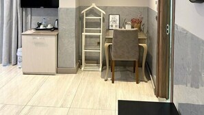 A compact living space with a kitchenette, a TV, a desk with a chair, and a clock on the wall. - Yankı Hotel (Bursa)