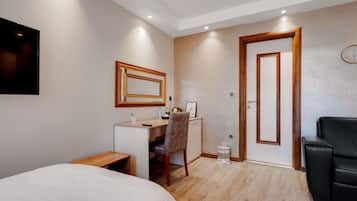 Habitación de hotel con cama, escritorio, silla, una mesita y un cubo de basura.