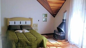 Um quarto com cama, teto de madeira, lareira e janela com cortinas.