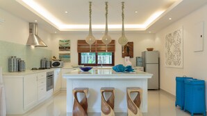 Une cuisine moderne avec un îlot central, des tabourets en bois, un réfrigérateur et un évier.