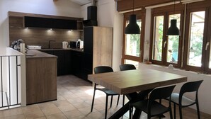 A modern kitchen with a wooden table and chairs, a built-in oven, and a window with a view of greenery.