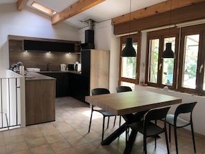 Een moderne keuken met een houten tafel en stoelen, een inbouwoven en een raam met uitzicht op groen.