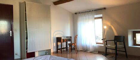 A bedroom with a bed, a desk, two chairs, a window with curtains, and a balcony.