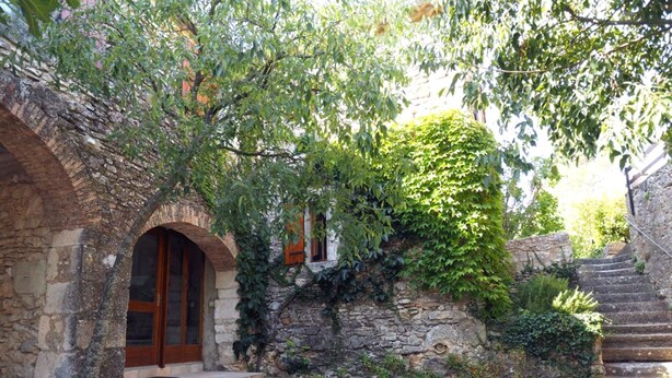 A stone building with an arched entrance, a stone staircase, and a paved courtyard.
