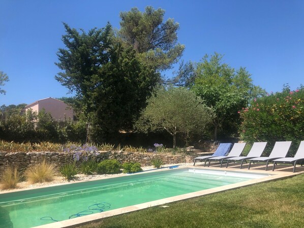 Una piscina con sillas de descanso, rodeada de follaje y un muro de piedra.