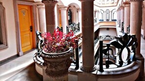 A grand hallway with classical architecture, including columns and arches, leading to a bright room with a large window. - Hotel Hacienda Los Narcisos (San Juan de los Lagos)