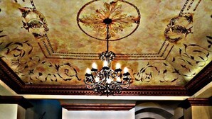 A grand lobby with a chandelier, a staircase, and a glass table with a vase of flowers. - Hotel Hacienda Los Narcisos (San Juan de los Lagos)