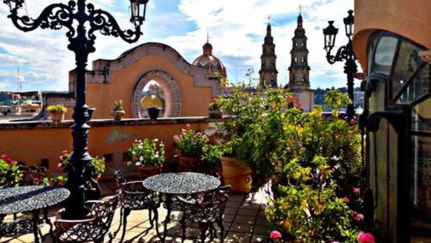 An outdoor patio with tables and chairs, surrounded by potted plants and flowers. - Hotel Hacienda Los Narcisos (San Juan de los Lagos)