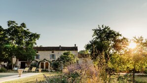Ein traditionelles Steinhaus mit Ziegeldach, umgeben von einem gepflegten Garten mit verschiedenen Pflanzen und einem Weg zum Eingang.