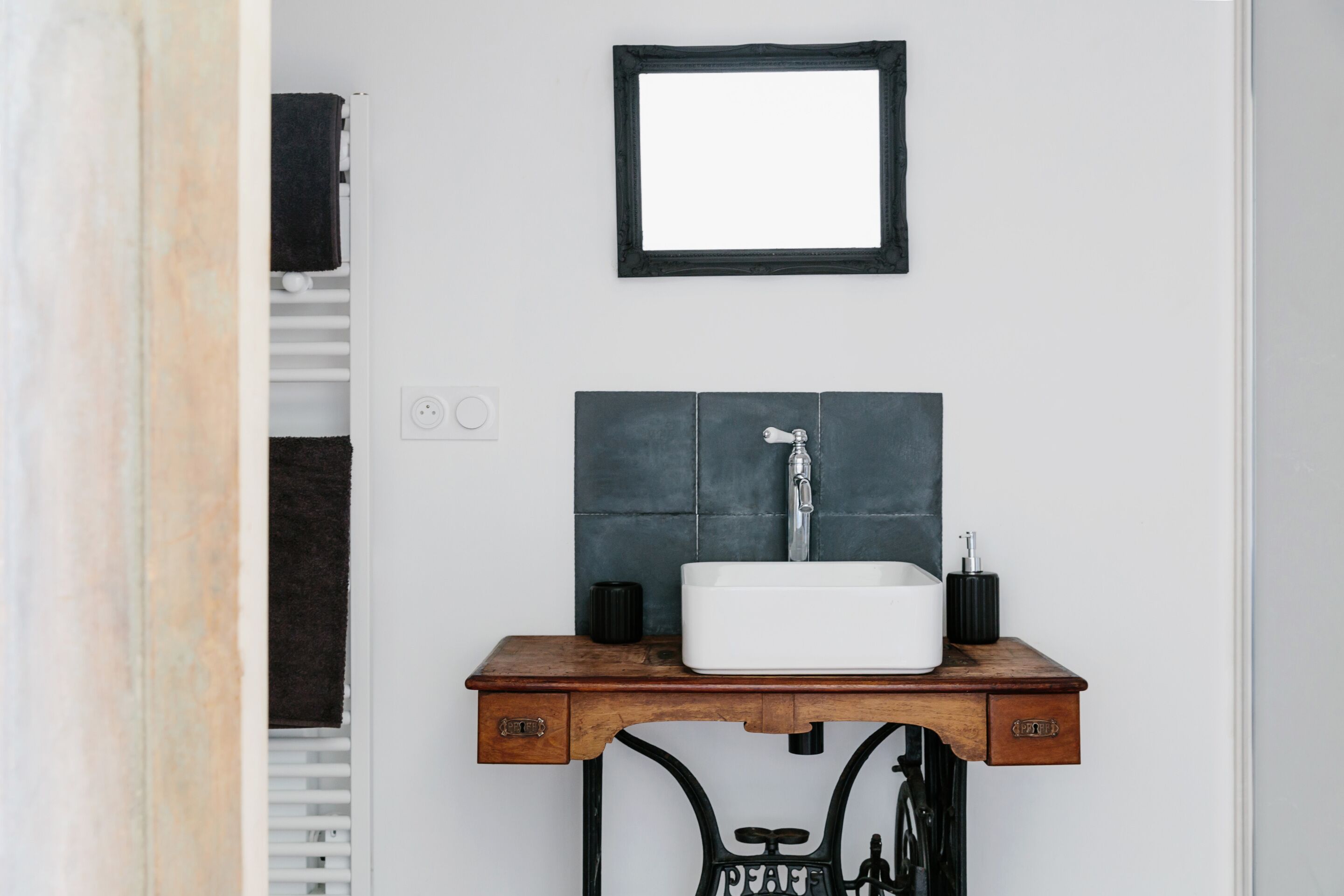 A bathroom with a white sink, a black-framed mirror, and a wooden vanity.