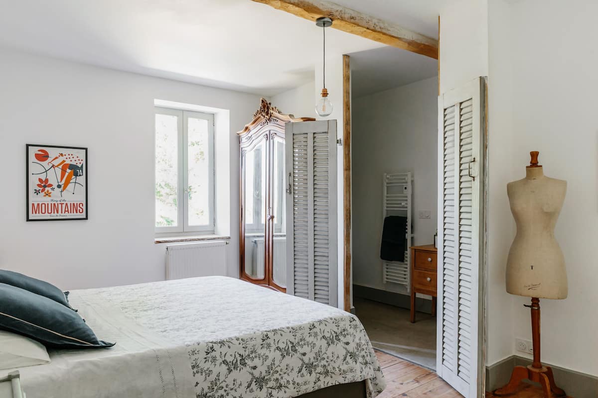 A bedroom with a bed, a mannequin, a dresser, and a window.