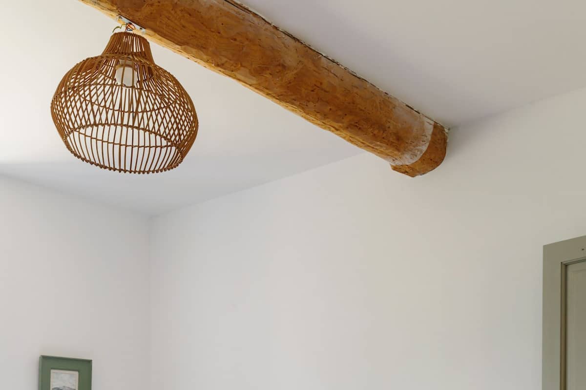 A bedroom with a bed, two pillows, a hanging light fixture, a bedside table with a lamp, and a door.