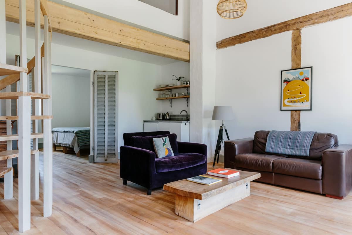 A spacious living room with a wooden staircase, a purple sofa, a brown sofa, and a coffee table.