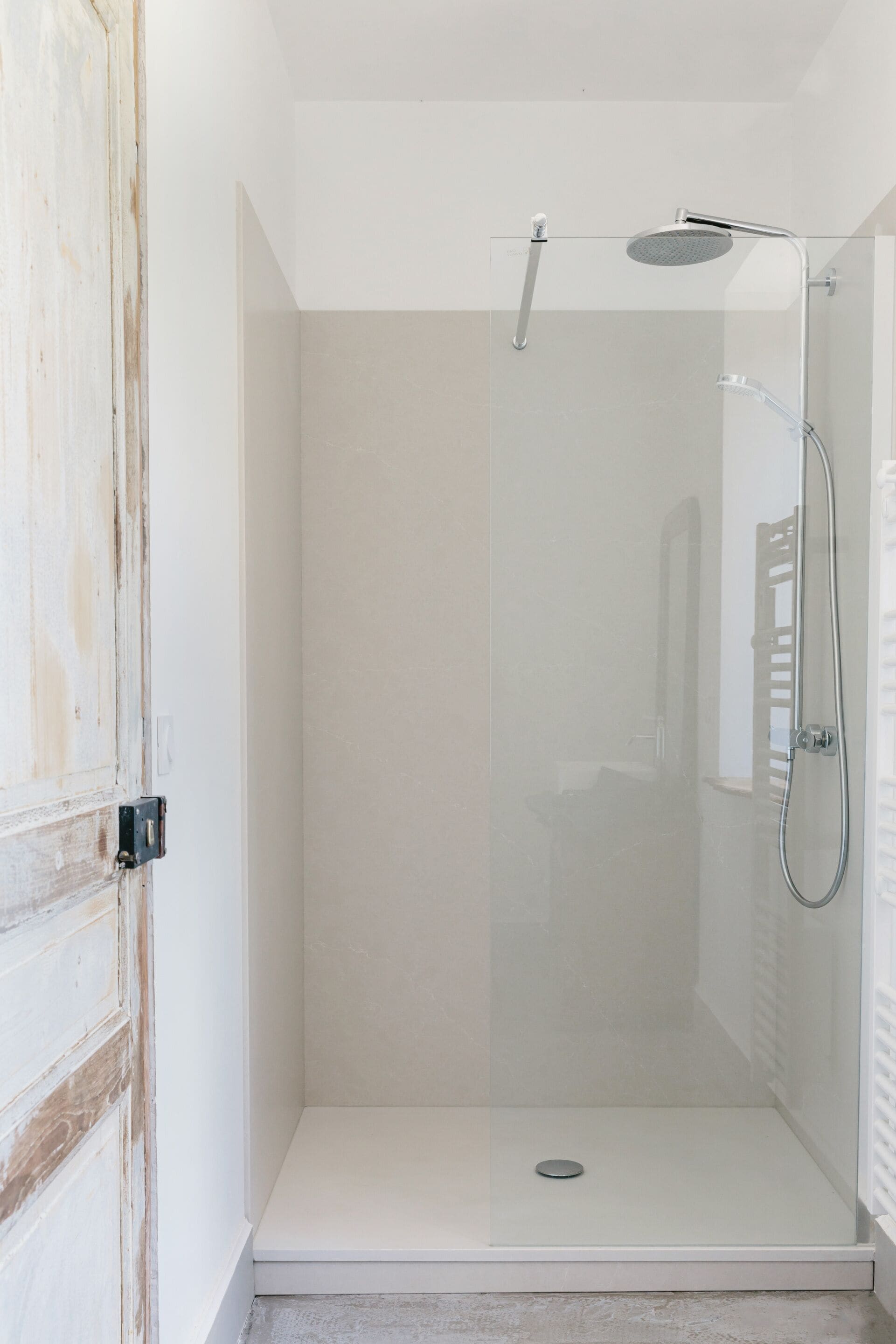Une douche fermée par des parois en verre, dotée d’un pommeau de douche à main et d’un pommeau de douche fixe au plafond.