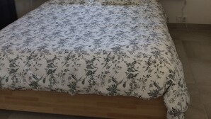 Ein Schlafzimmer mit einem hölzernen Kopfteil, einem Bett mit floralem Bettzeug, zwei Nachttischen mit Lampen und einem Fenster mit Vorhängen.