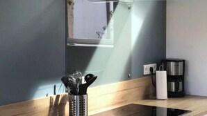 Eine moderne Küche mit einer Edelstahl-Dunstesse, einer hängenden Pendelleuchte, einer Kaffeemaschine und einem Messerblock auf der Arbeitsplatte.