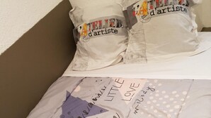 A bed with a quilt featuring text and patterns, and pillows with a similar design. - Jaude Stay Aparthotel (Clermont-Ferrand)
