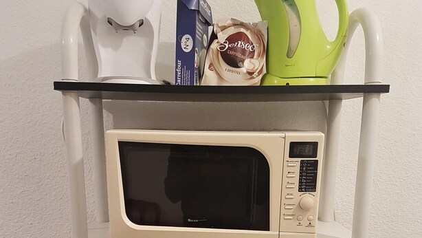 A kitchen shelf with a microwave, a coffee maker, a green kettle, a box of coffee pods, and a red plate set. - Jaude Stay Aparthotel (Clermont-Ferrand)