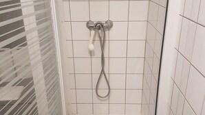 A glass-enclosed shower with a handheld showerhead and a floor drain. - Jaude Stay Aparthotel (Clermont-Ferrand)