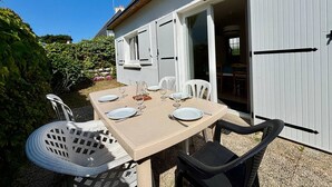 A dining area with a table set for four, white chairs, and a white fence in the background. - Quiet 4-room house, near St Colomban beach, pets allowed (Carnac)