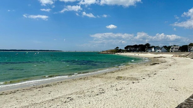 A beach with clear blue water, sandy shore, and houses in the background. - Quiet 4-room house, near St Colomban beach, pets allowed (Carnac)