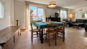 A dining area with a table set for four, a sofa, and a television in the background. - Quiet 4-room house, near St Colomban beach, pets allowed (Carnac)