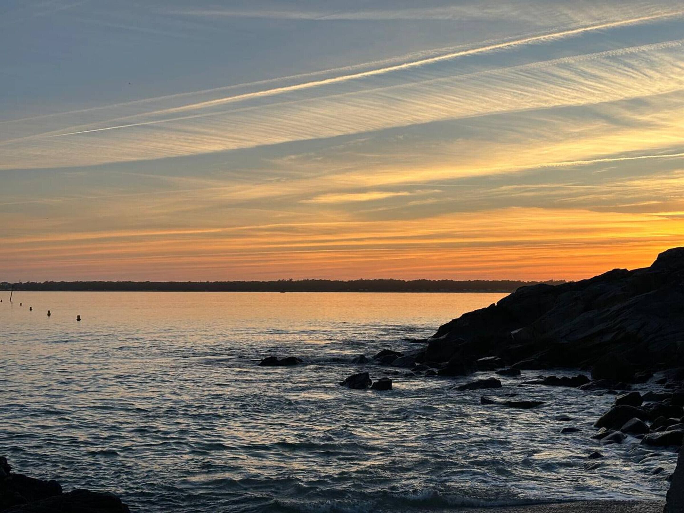A coastal sunset with calm waters and rocky outcrops.