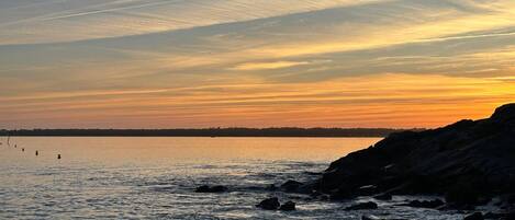 A coastal sunset with calm waters and rocky outcrops.