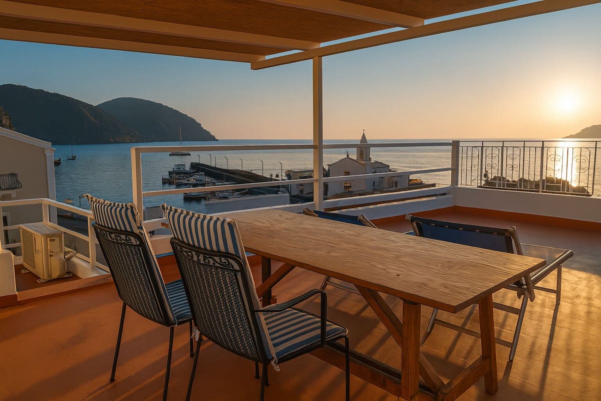 A balcony with a wooden table and chairs, overlooking a body of water and a distant shoreline.