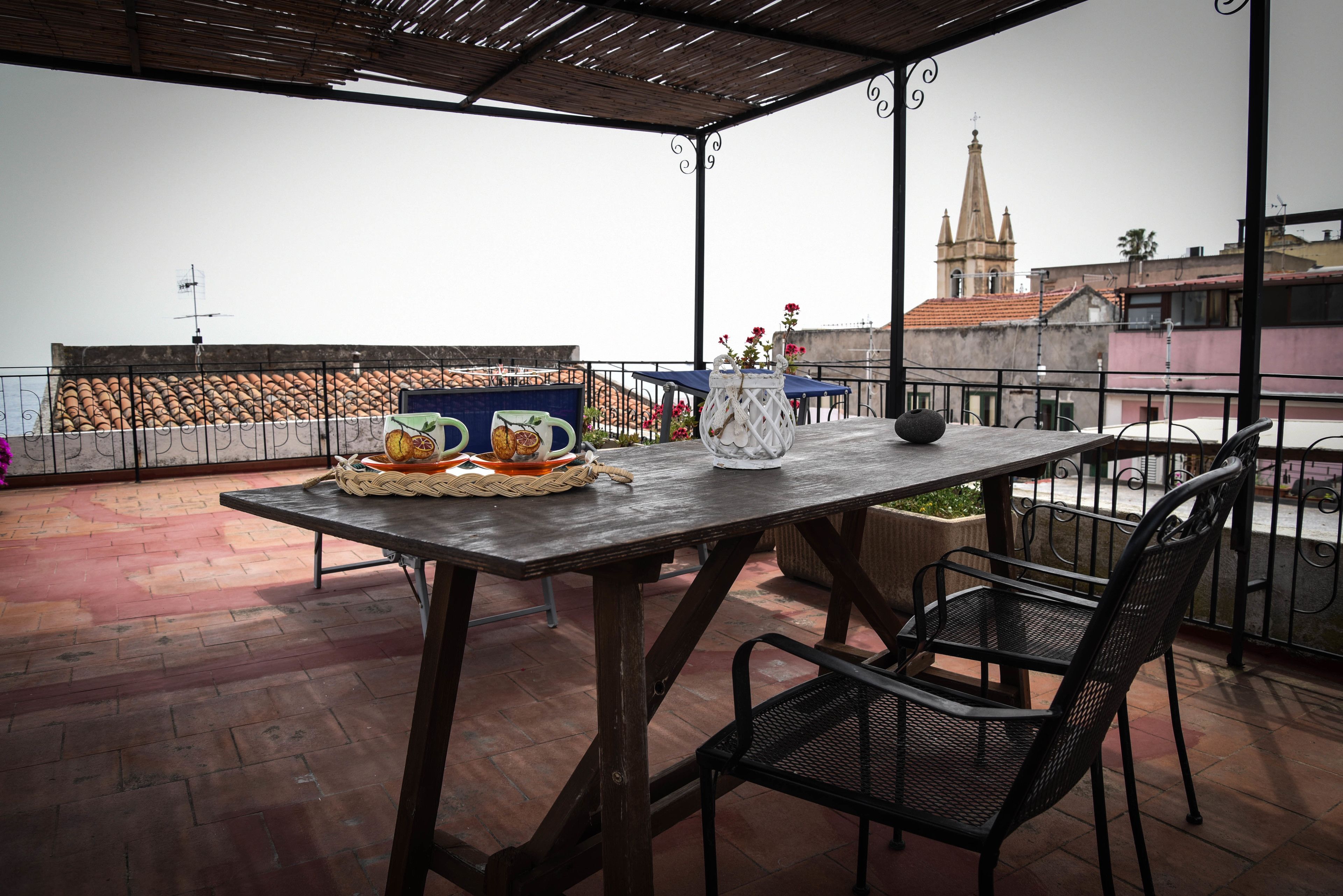 A terrace with a table and chairs, a decorative pitcher, and a basket of bread.