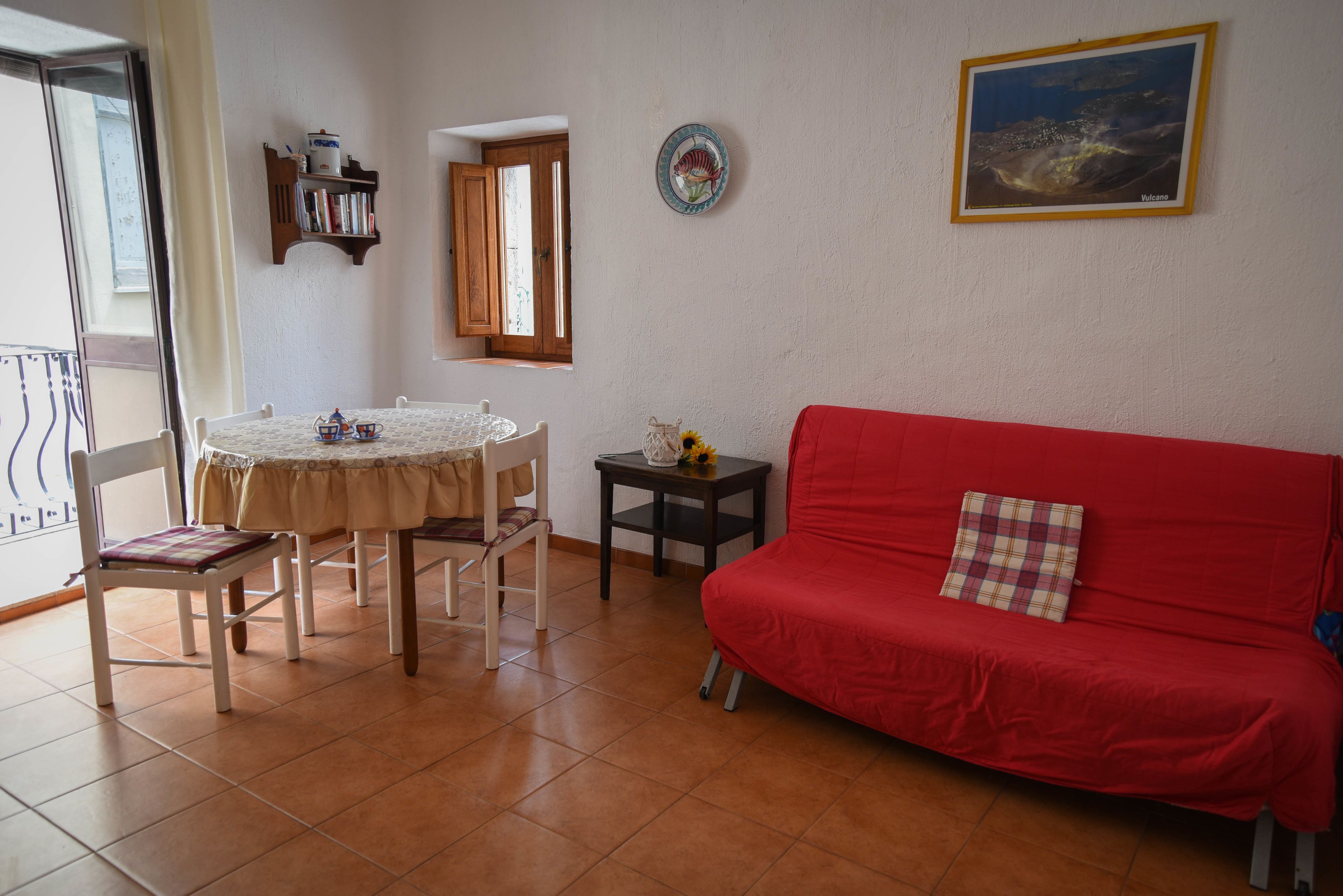 A dining area with a round table, chairs, a red sofa, and a small side table.