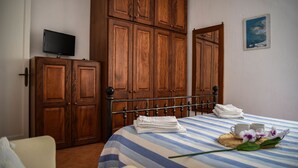 A bedroom with a bed, wooden wardrobe, a television on the wall, and a painting. - Casa Giuliana (Lipari)
