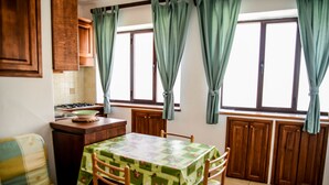 A kitchen with a dining table, chairs, a sofa, and wooden cabinets. - Casa Giuliana (Lipari)