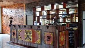 A reception desk with a brick wall backdrop, a tiled floor, and a ceiling with wooden beams. - Paradis Vert (Krabi)