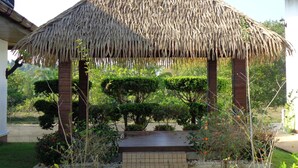 A thatched-roof gazebo in a landscaped garden with trimmed bushes and a paved walkway. - Paradis Vert (Krabi)