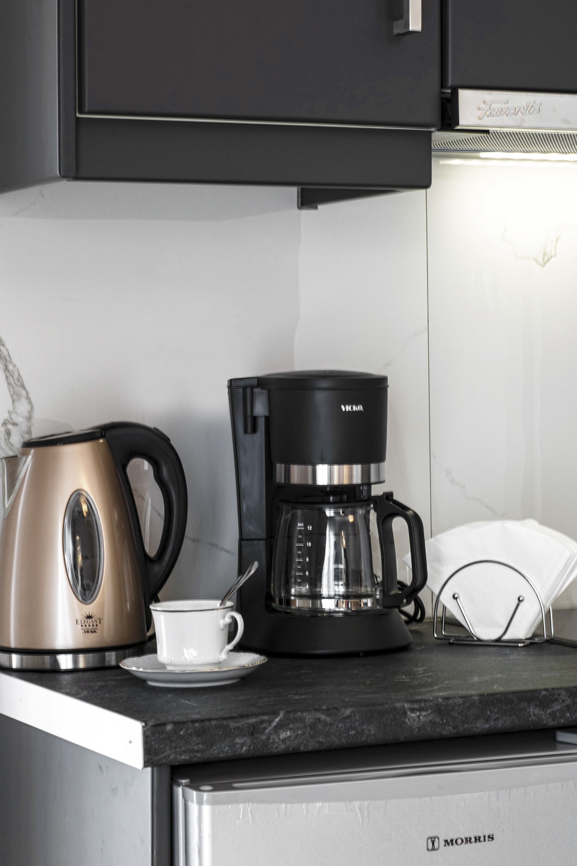 Una cocina con una cafetera, un hervidor y una taza sobre la encimera.