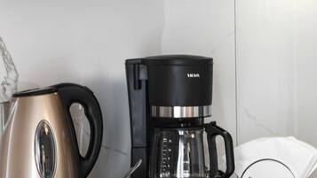 Una cocina con una cafetera, un hervidor y una taza sobre la encimera.