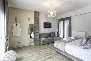 A modern bedroom with a large bed, a grey sofa, a wardrobe, and a hanging robe.