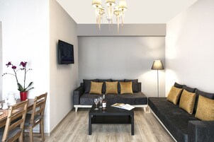 A modern living room with a grey sofa, a coffee table, a dining table with chairs, a TV mounted on the wall, and a floor lamp.