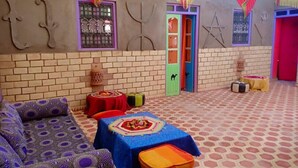 A room with a patterned floor, a sofa, a table with a colorful tablecloth, and a door with a star decoration. - Kasbah Casa Khamlia (Taouz)