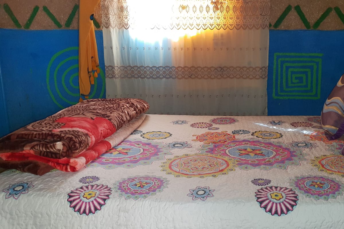 Una cama con una colcha estampada y colorida, un cabecero de madera y cojines decorativos.
